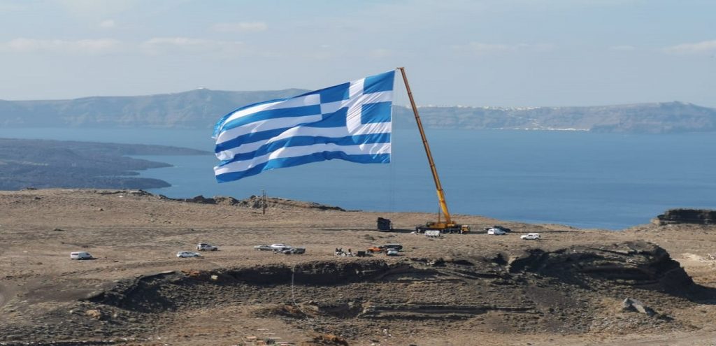 28η Οκτωβρίου: Η μεγαλύτερη ελληνική σημαία υψώθηκε με γερανό στη Σαντορίνη (βίντεο-φώτο)