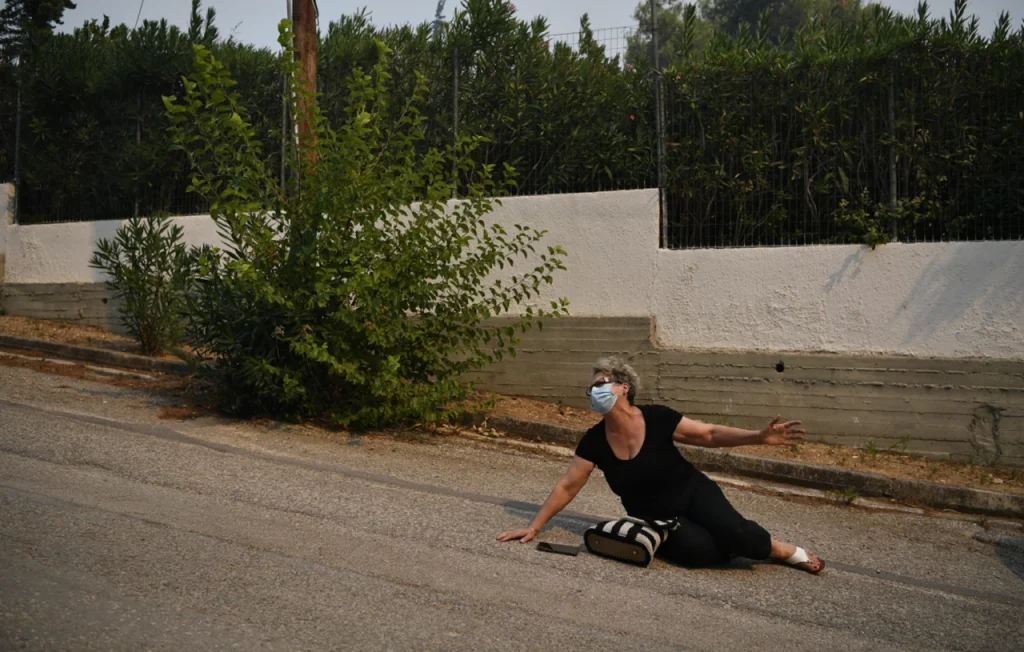 Συγκλονιστική φωτογραφία από τη φωτιά στην Αττική: Γυναίκα πεσμένη στο δρόμο βλέπει τις φλόγες να «καταπίνουν» τα πάντα